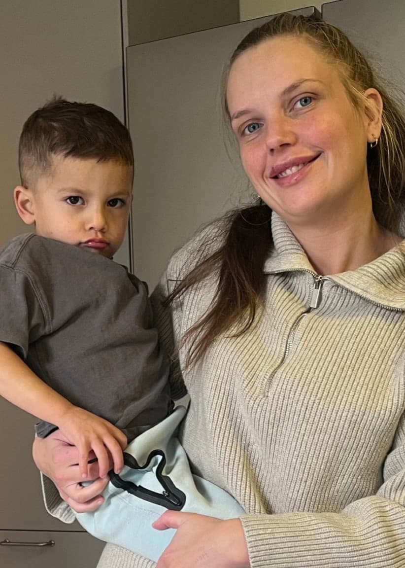 Fyrbarnsmamman Lina håller ett av sina barn i famnen i ett hem. På vänster sida syns ett annat barn vid ett bord med färgglada leksaker.
