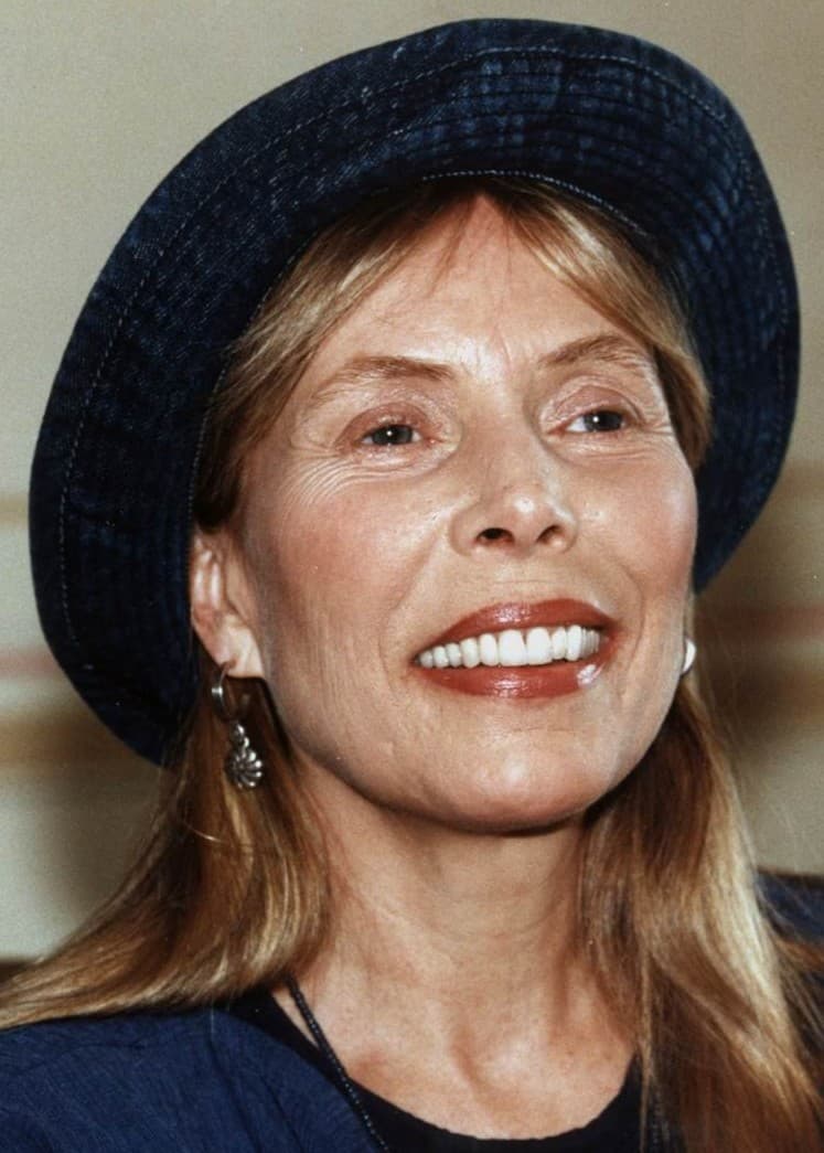 En gammal Joni Mitchell i svarta kläderoch flätor sitter och sjunger 