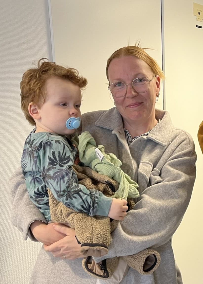 Familjen Saetran står inomhus i en ljus korridor. Två vuxna håller varsitt barn i famnen. 