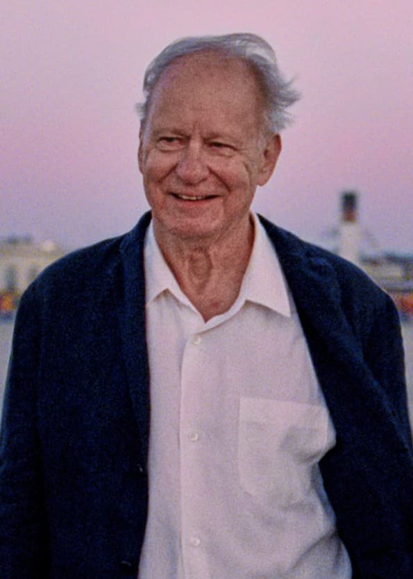 Stellan Skarsgård och Renate Reinsve står i ett rum, klädda i mörka kläder. Skarsgård håller en öppen låda medan Reinsve tittar mot honom. Bakgrunden visar en vit vägg med en tavla.