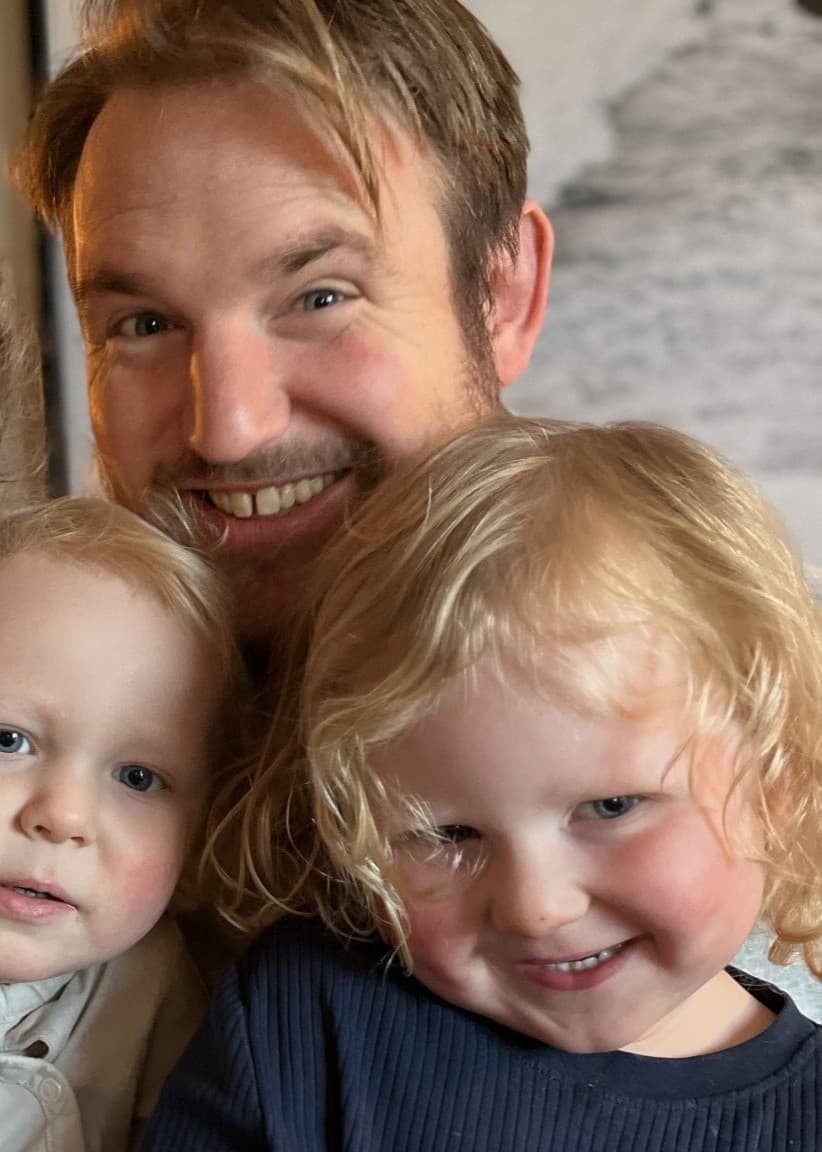 Amanda och Emil Norberg sitter tillsammans med sina barn, Molle och Beppe, i ett hem med en tänd lampa och en tavla på väggen i bakgrunden. Familjen är klädd i vardagskläder.