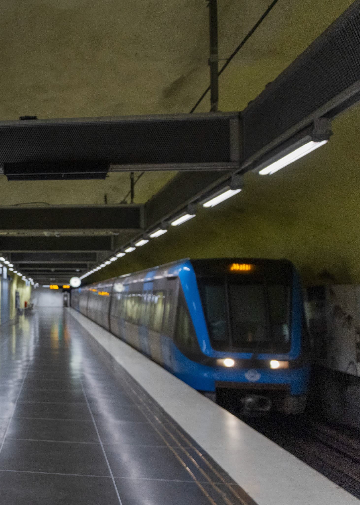Till vänster syns en person som nyser, och till höger en tunnelbanevagn som passerar en station i hög fart.