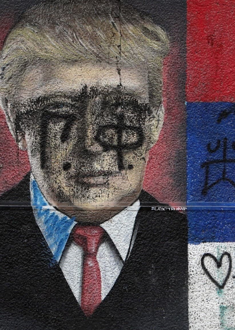 A man passes by graffiti depicting the US President Donald Trump and Serbian flag vandalized with paint,