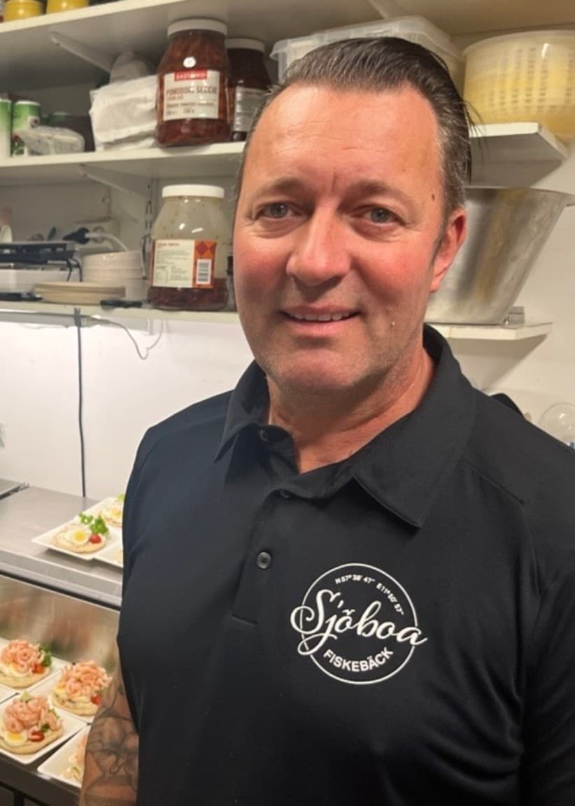 Delad bild. Till vänster syns en skylt utanför ett café med text som uppmanar att rapportera gäster som äter medhavd mat. Till höger syns caféägaren Stefan Börjesson stående i köket i svart t-shirt med smörgåsar i bakgrunden.