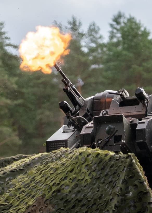 Stridsfordon avfyrar ett skott under militärövning i skogsmiljö.