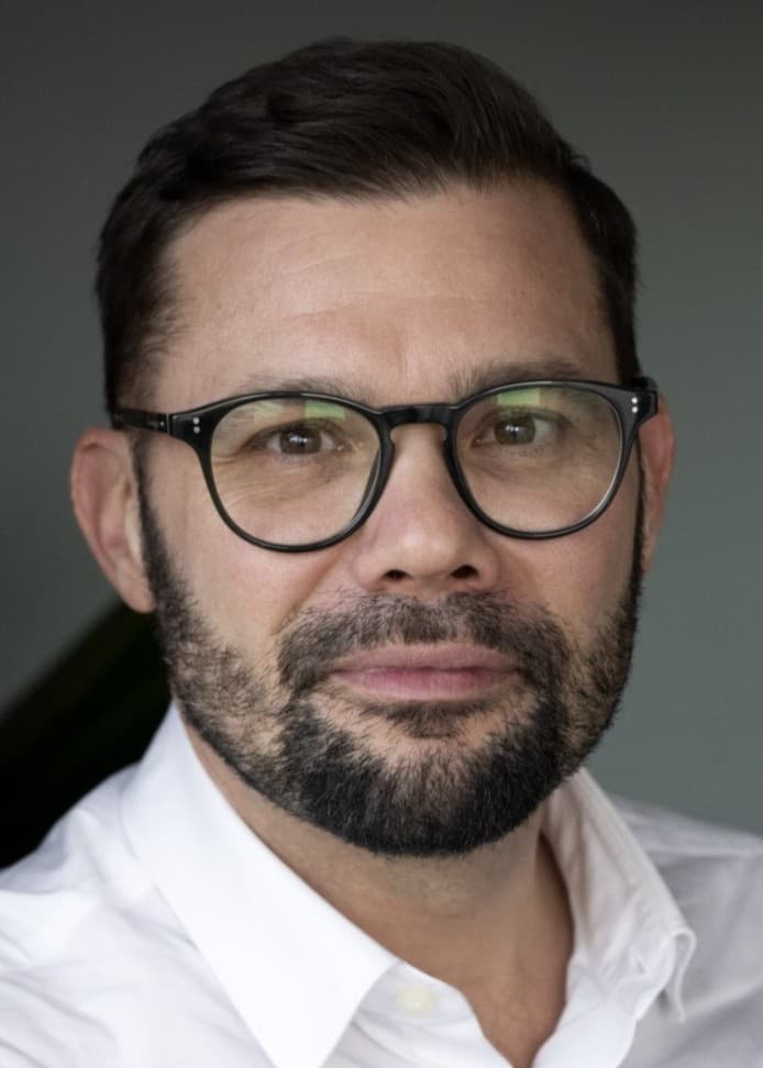 Magnus Demervall står mot en vit vägg iklädd vit skjorta. 