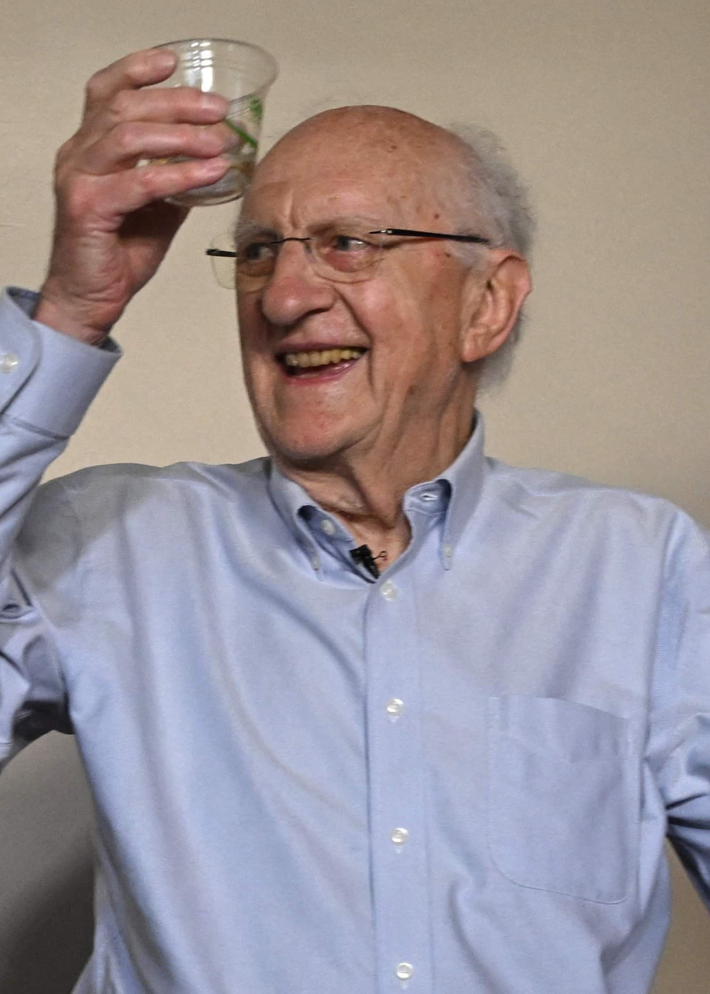 Professor Emeritus John Clarke höjer ett plastglas. Han har på sig en blank ljusblå skjorta.