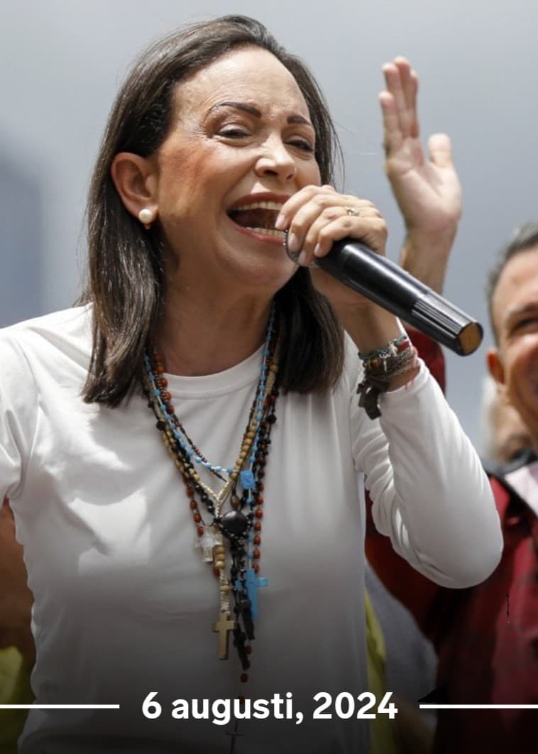 Maria Corina Machado och Edmundo Gonzalez håller upp sina händer bland supportrar. Maria talar i en mikrofon.