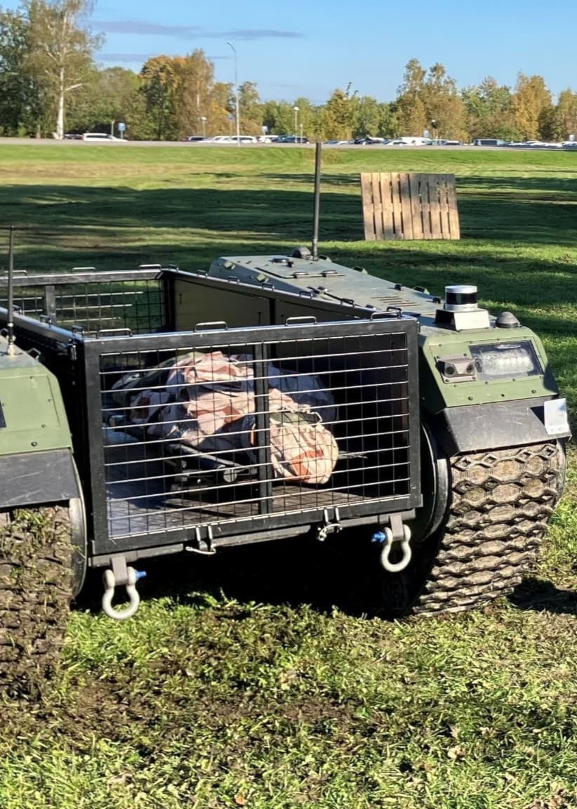 En man styr en grön markdrönare med larvfötter på en gräsbevuxen öppen yta.