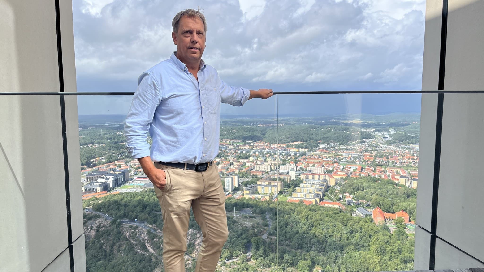 Niklas Jakobsson, utvecklare av besöksvåningen på Karlatornet, står vid en glasvägg med utsikt över Göteborgs stad och grönområden under en molnig himmel.