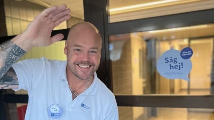 En glad man hälsar med handen utanför porten till ett lägenhetshus i Göteborg