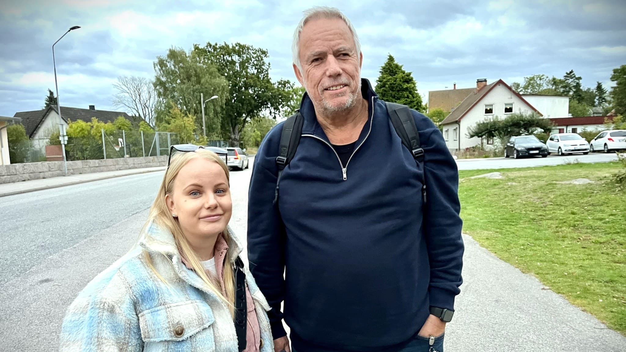 Anders Pettersson och Julia Blackby står vid en väg i Karlskrona skärgård, omgivna av hus och grönska under en molnig himmel.