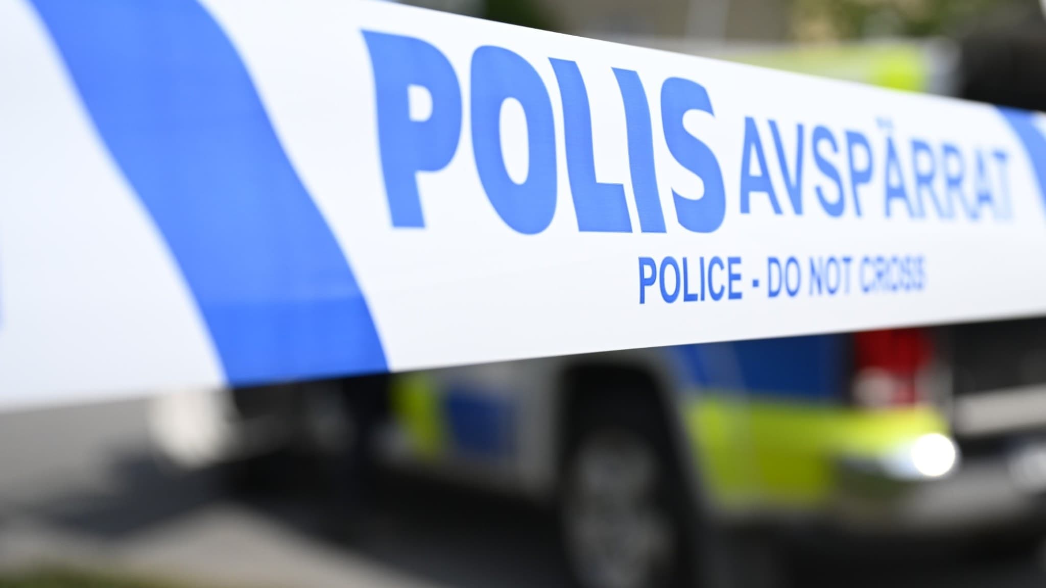En polisavspärrning med blåvit tejp som det står 'Polisavspärrat' på, framför en polisbil i Huddinge. Polisen undersöker ett misstänkt farligt föremål vid Frivården.