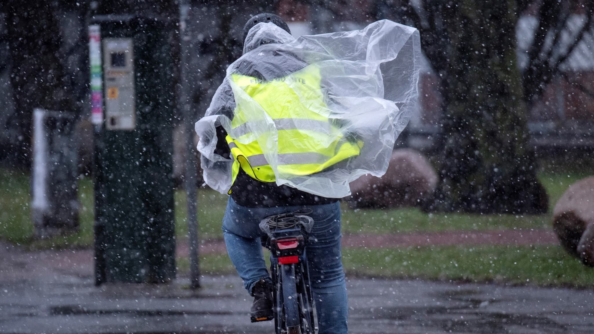 En cyklist i Malmö kämpar mot snöblandat regn och kraftig sidvind. Personen bär en regnponcho och en reflexväst. Vädervarningen: Nu kommer stormen Amy till Kronoberg
