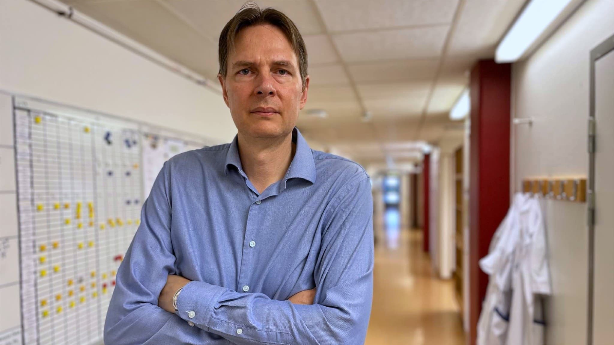 Christian Blomqvist, smittskyddsläkare i Kronoberg, står med armarna i kors i en sjukhuskorridor med ljusa väggar och en whiteboard fylld med anteckningar i bakgrunden. Kronobergare bland de smittade efter listeriautbrott på krog