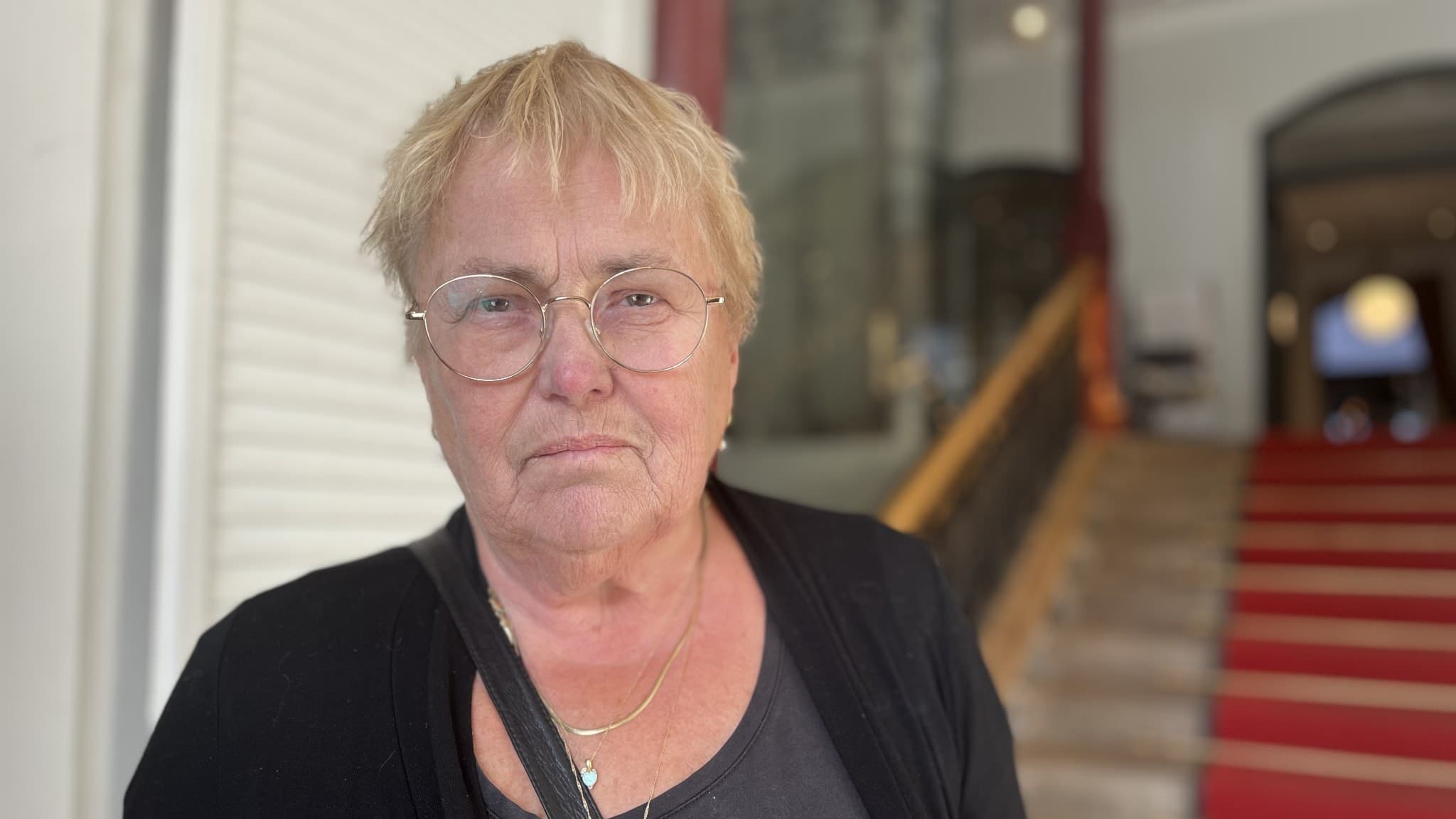 Carin Nilsson står inomhus framför en trappa med röd matta i Umeå. Hon bär en svart tröja och ett halsband.