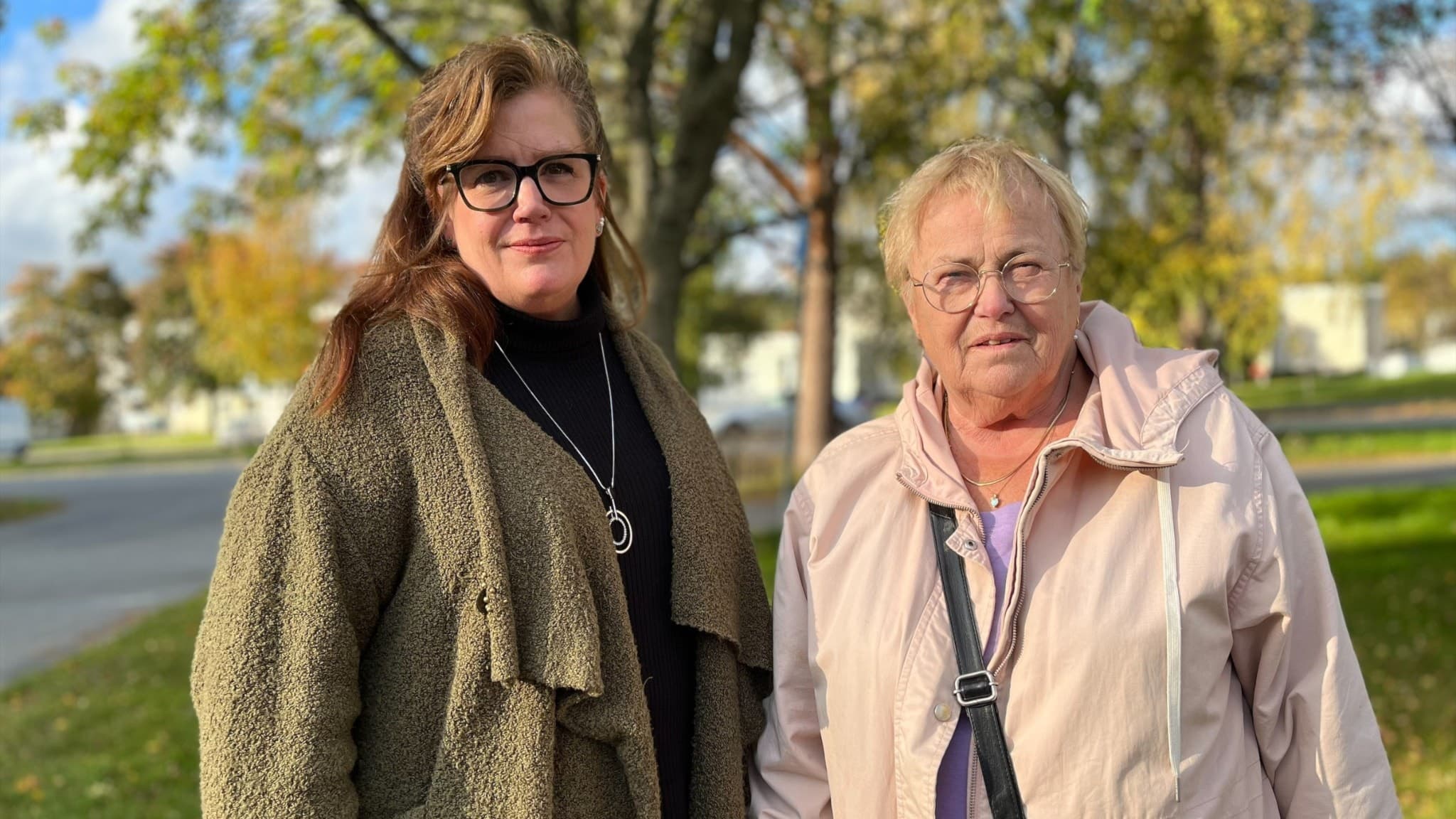 Veronica Kerr och Carin Nilsson står vid en gräsmatta och tittar in i kameran. De har höstjackor på sig och i bakgrunden syns grön-gula träd. 