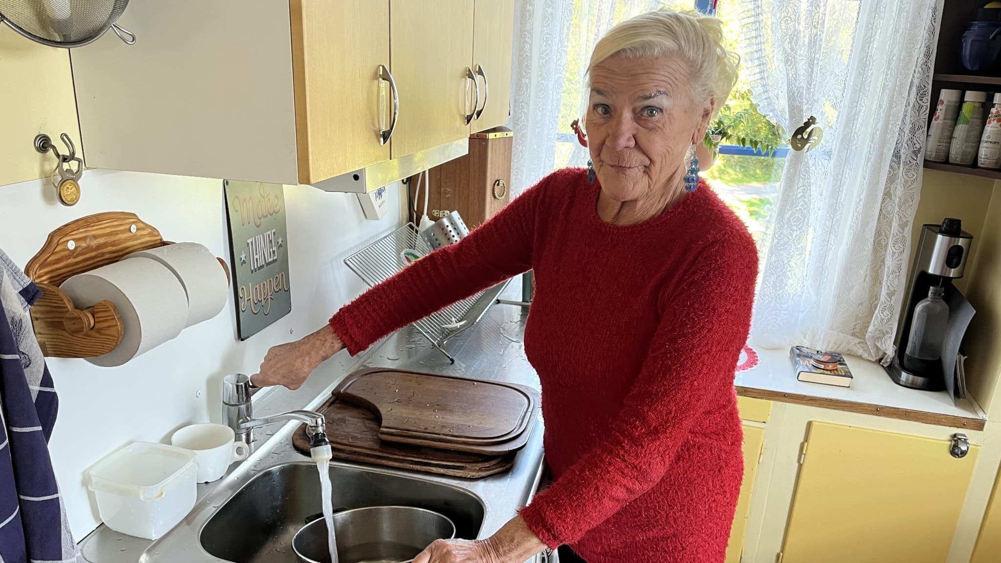 Christina Gyllenberg från Kramfors står vid en diskbänk i ett kök och håller i en kran. Köket har ljusa skåpluckor, en vit gardin och köksredskap synliga i bakgrunden.