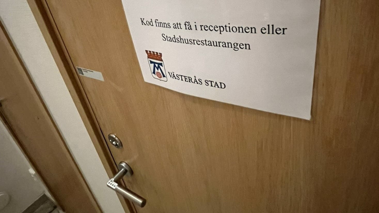 En stängd dörr med en lapp som informerar om att man kan få en kod till toaletten i receptionen. 