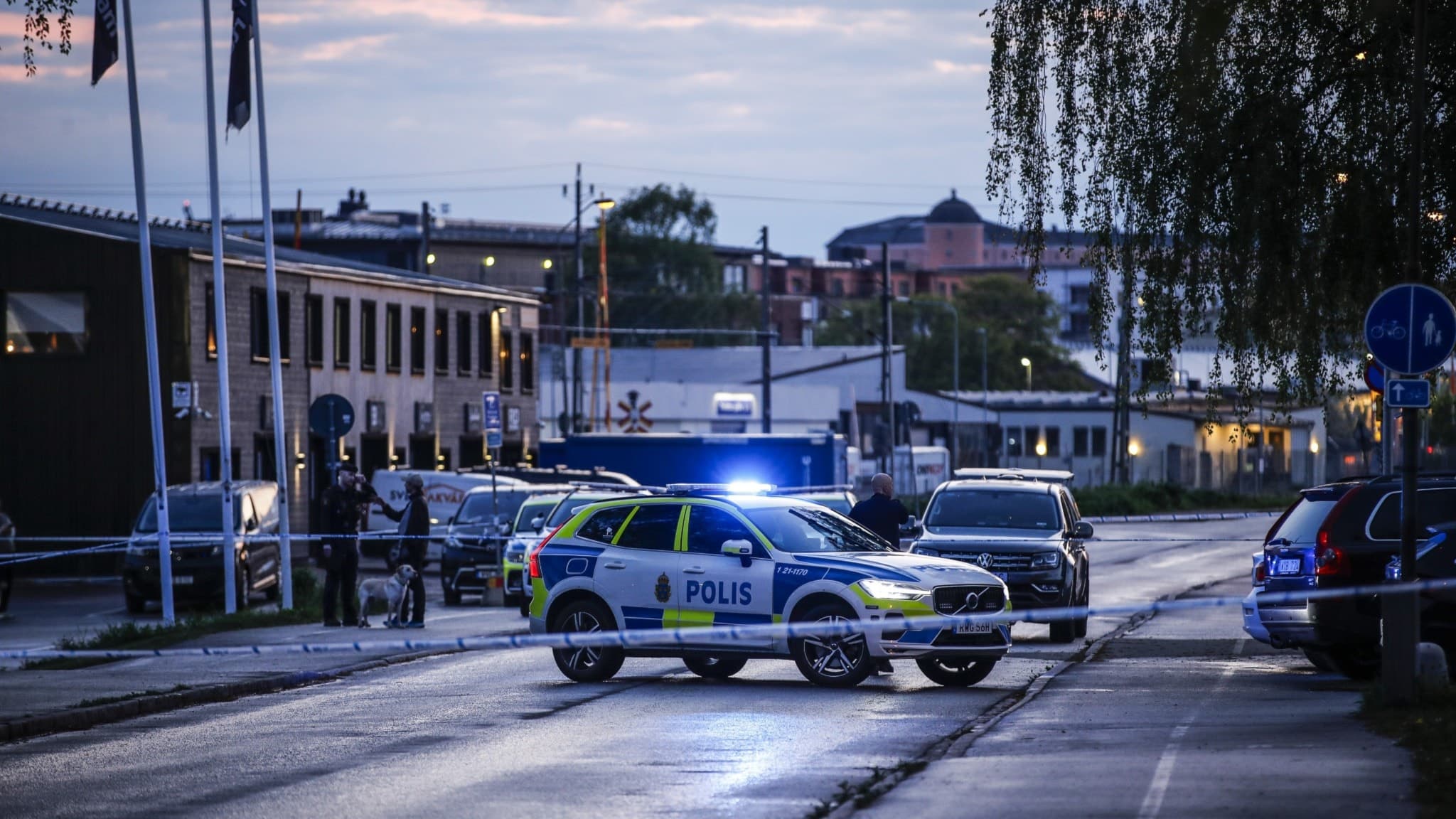 En polisbil med blåljus spärrar av en gata i Boländerna, centrala Uppsala, efter larm om skottlossning. Området är avspärrat och flera byggnader syns i bakgrunden under skymning.