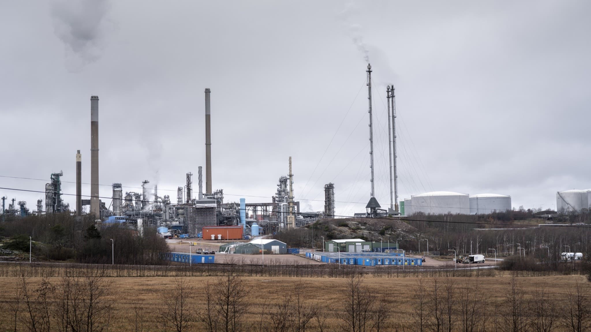 Industribyggnader vid Preemraff i Lysekil med höga skorstenar under en grå himmel. Raffinaderiet är föremål för rättsliga prövningar kring planerad utbyggnad.