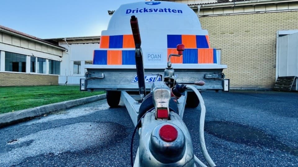 En dricksvattentank står parkerad vid Birger Sjöbergsgymnasiet, som är stängt på grund av en upptäckt läcka. Slangar och kopplingar syns i förgrunden.