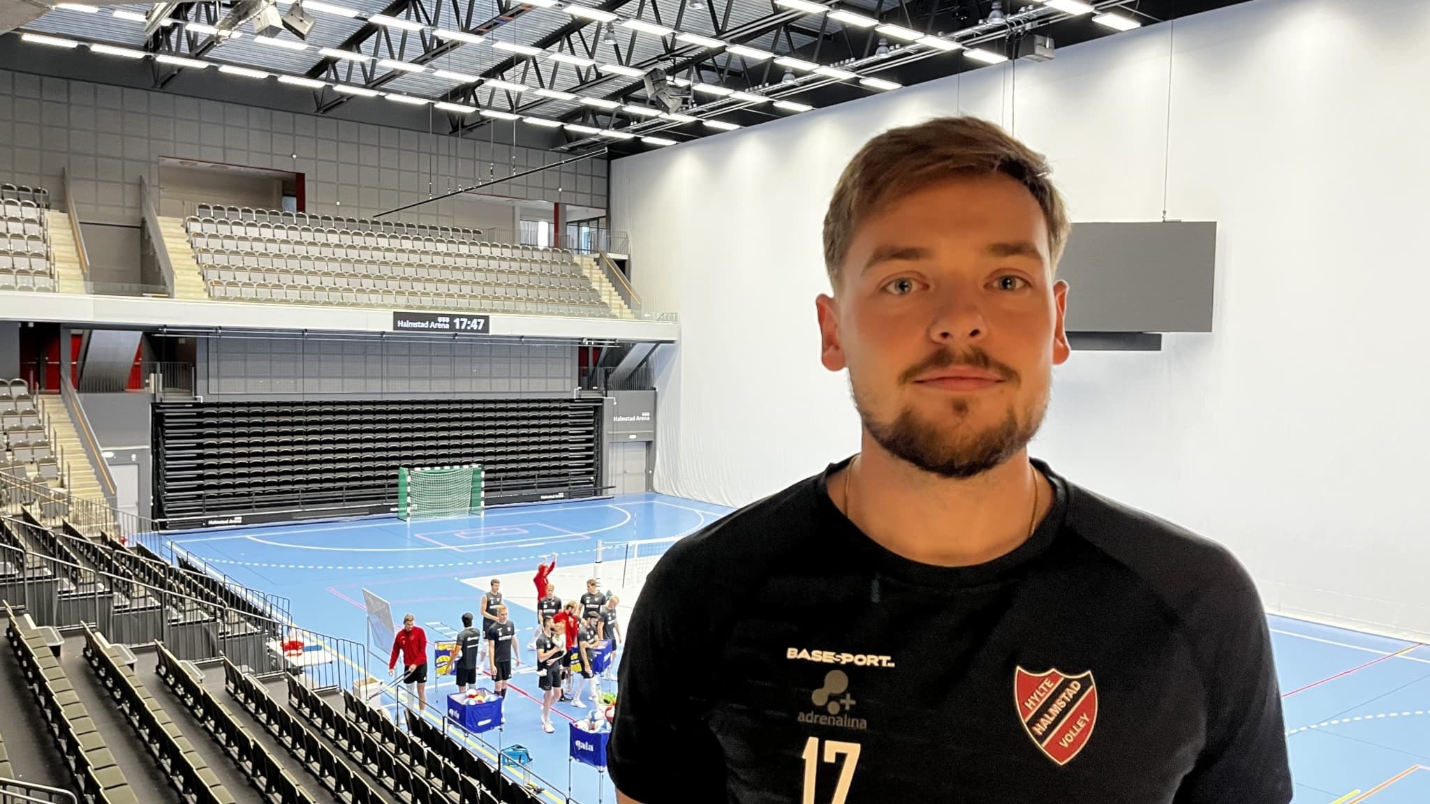 Volleybollspelaren Edvin Svärd i Hylte/Halmstad står i en arena med spelare som värmer upp i bakgrunden