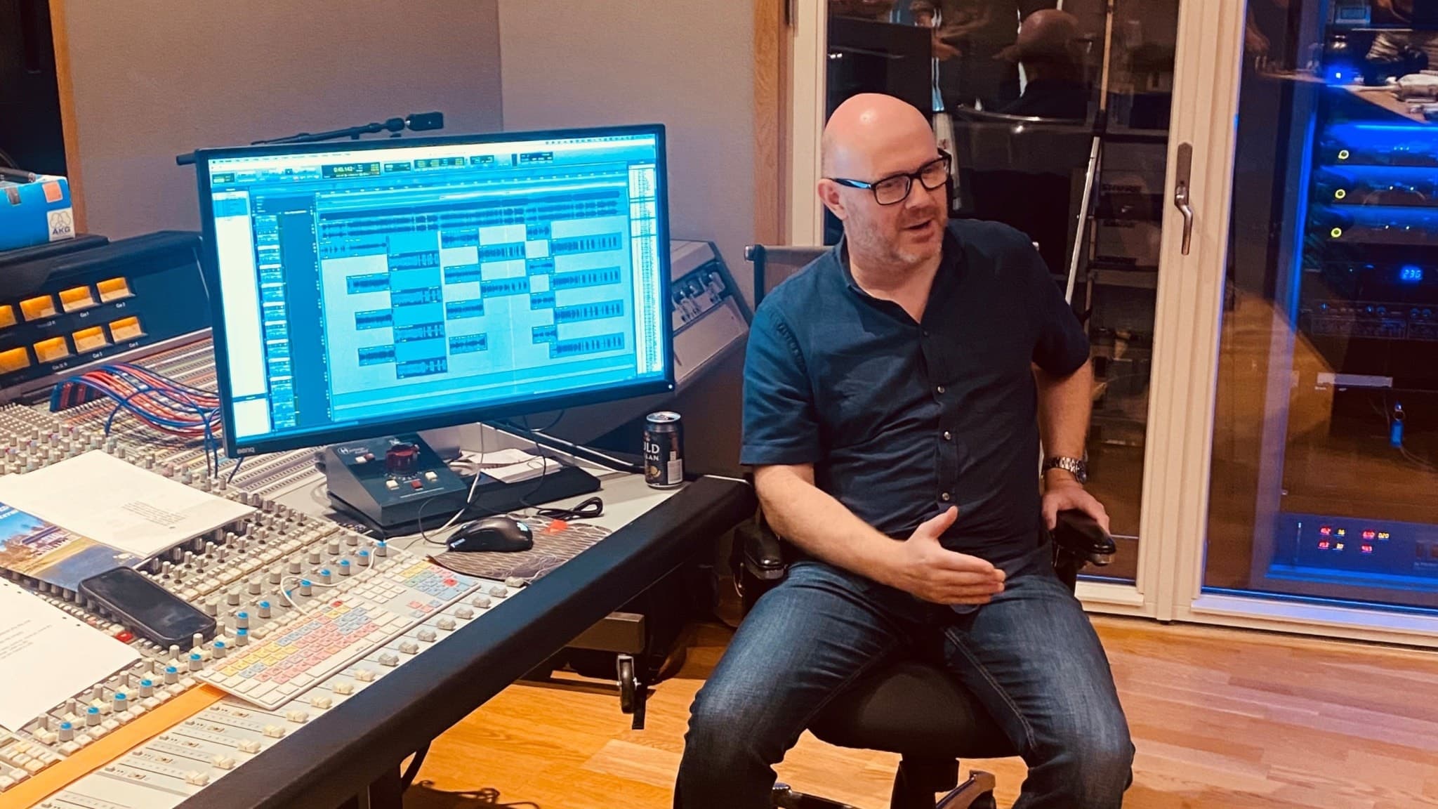 Fredrik Larnemo sitter i en musikstudio framför en stor mixerbord och en datorskärm med musikprogram, omgiven av avancerad inspelningsutrustning.