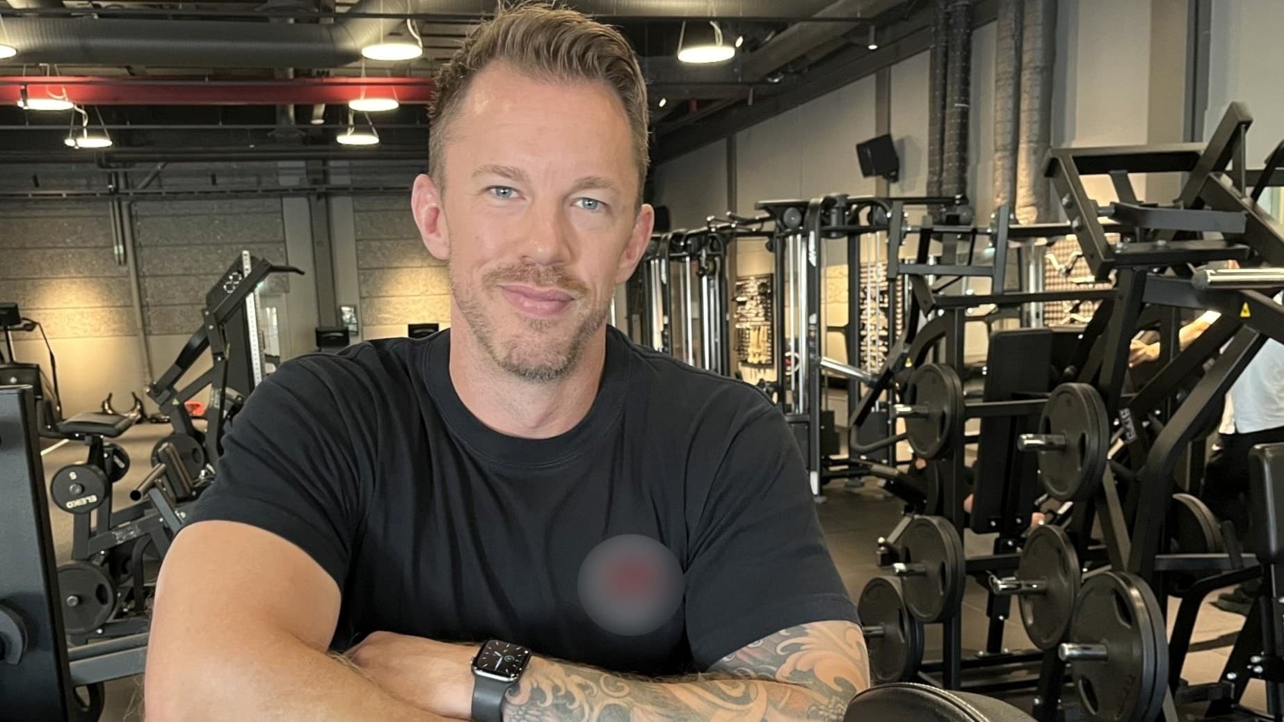 Patrik Stovell står i ett gym med träningsmaskiner i bakgrunden, iklädd svart t-shirt och visar upp sina tatuerade armar. Han är aktuell i den nya säsongen av GVFÖ.