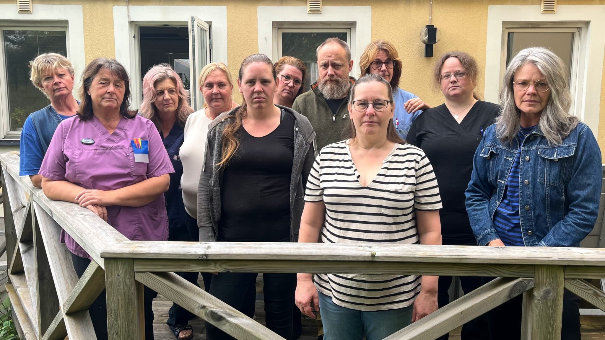 En grupp med hemtjänstpersonal från Fellingsbro står på en träveranda framför en gul byggnad. De visar blandade känslor inför en eventuell flytt som berör deras arbetsplats.