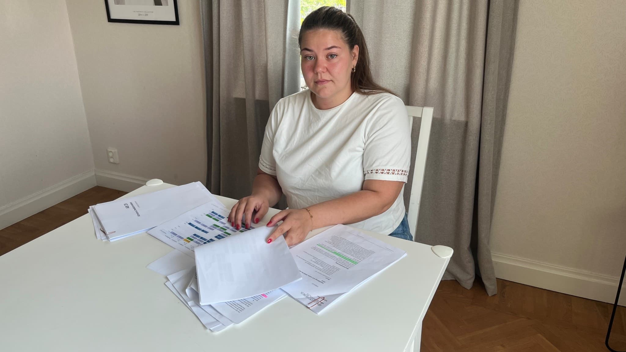 Sofie Pettersson, undersköterska i Lindesberg, sitter vid ett vitt bord och hanterar dokument i ett kontorsliknande rum med grå gardiner och en vit vägg med tavla.