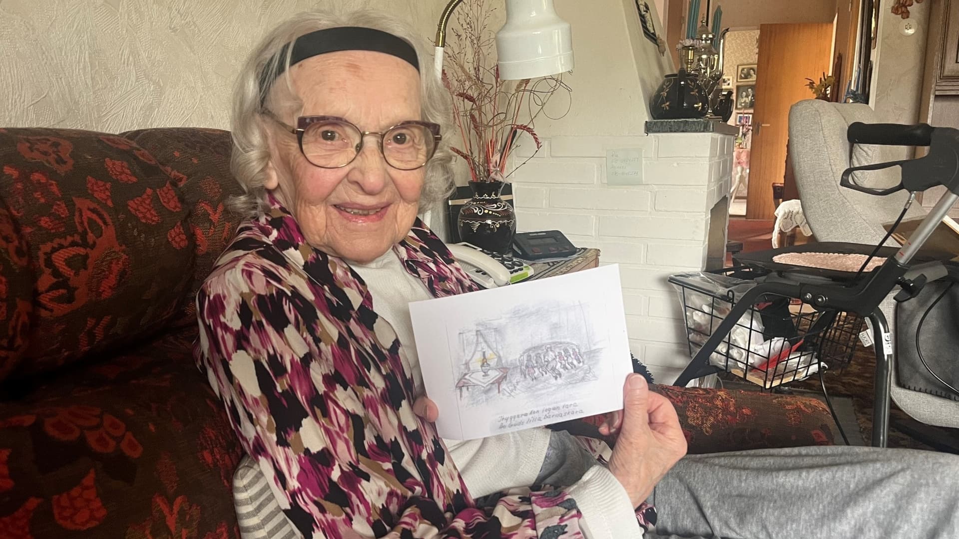 Vera Flink i sitt soffhörn, med en teckning hon gjort efter minnen från barndomen. 
