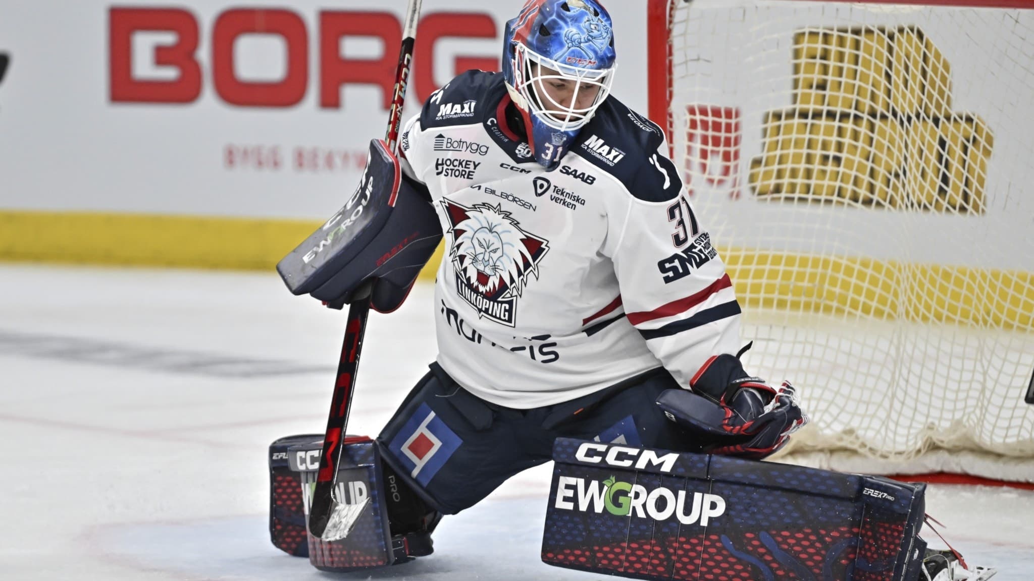 Linköpings målvakt Jesper Myrenberg i vit matchtröja och blå hjälm räddar pucken under en SHL-match. Ishockeymål syns i bakgrunden.
