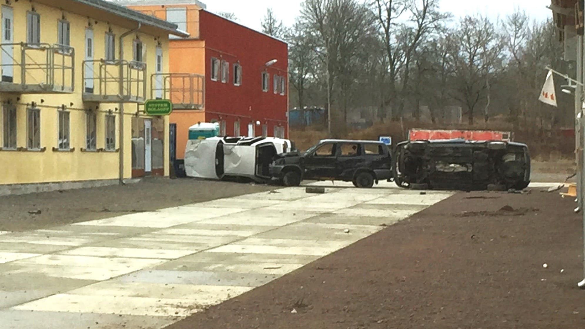 Bild från Markstridsskolan i Kvarn, Motala, visar tre bilar på sidan efter en olycka vid en militärövning. Byggnader i gul och röd färg syns i bakgrunden med grus och betong på marken.