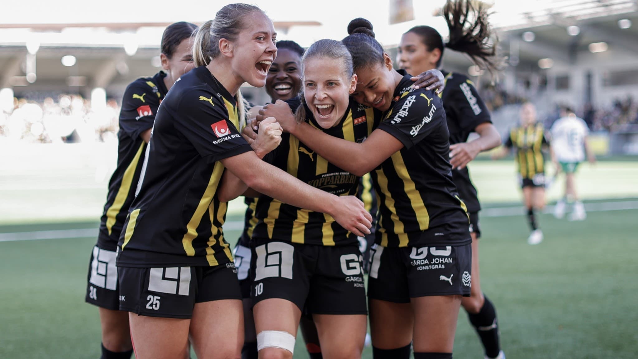 Häckens fotbollsspelare firar mål på Bravida Arena under matchen i damallsvenskan mot Hammarby. Anna Anvegård står i centrum efter att ha gjort 2-0, omgiven av glada lagkamrater i gulsvarta dräkter.