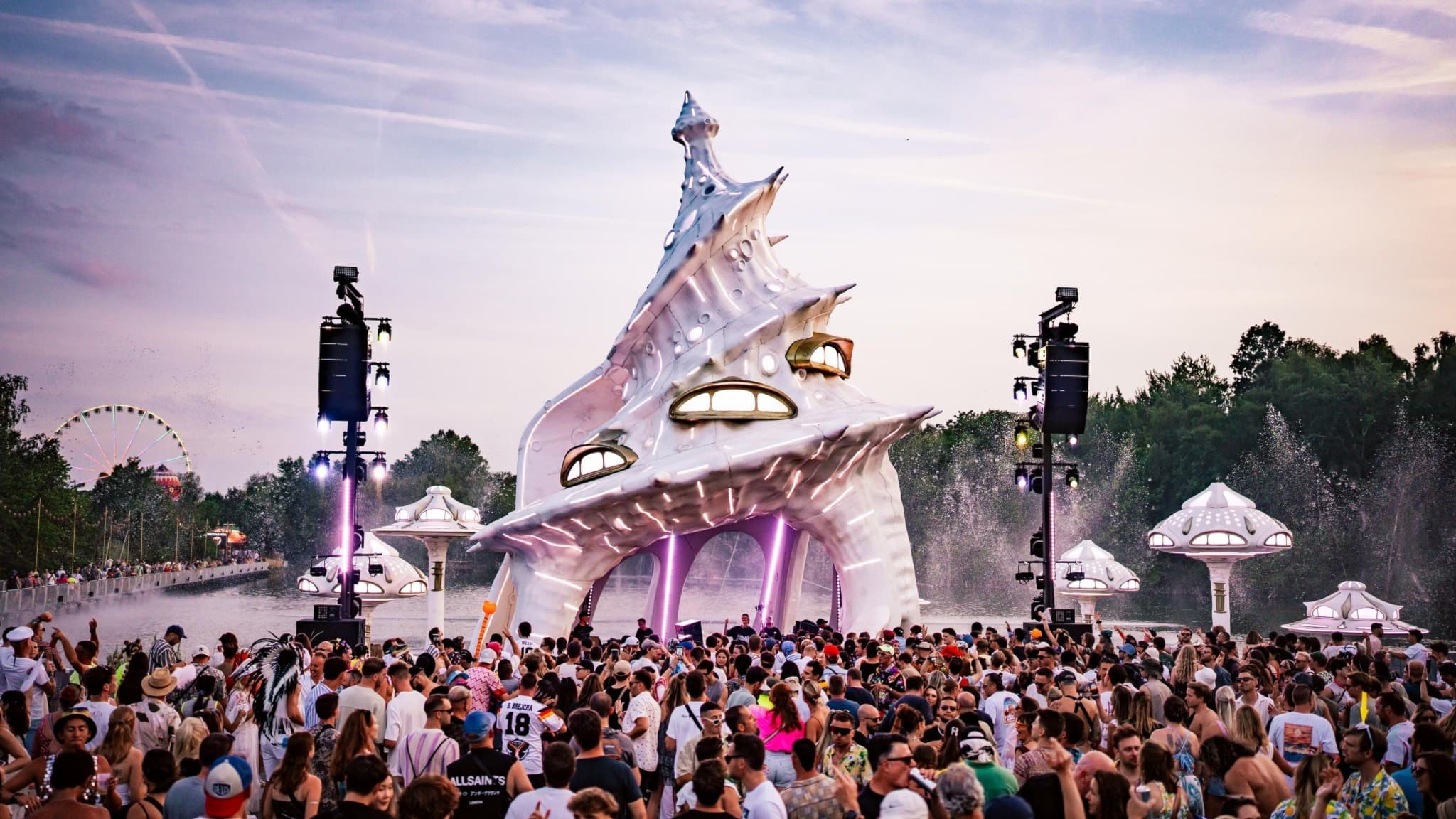 Fotot visar Planaxis scenen på Tomorrowland som ser ut som en stor vit snäcka i ett rymdlandskap med ett djbås i. framför snäckan som är scenen dansar massor av publik.