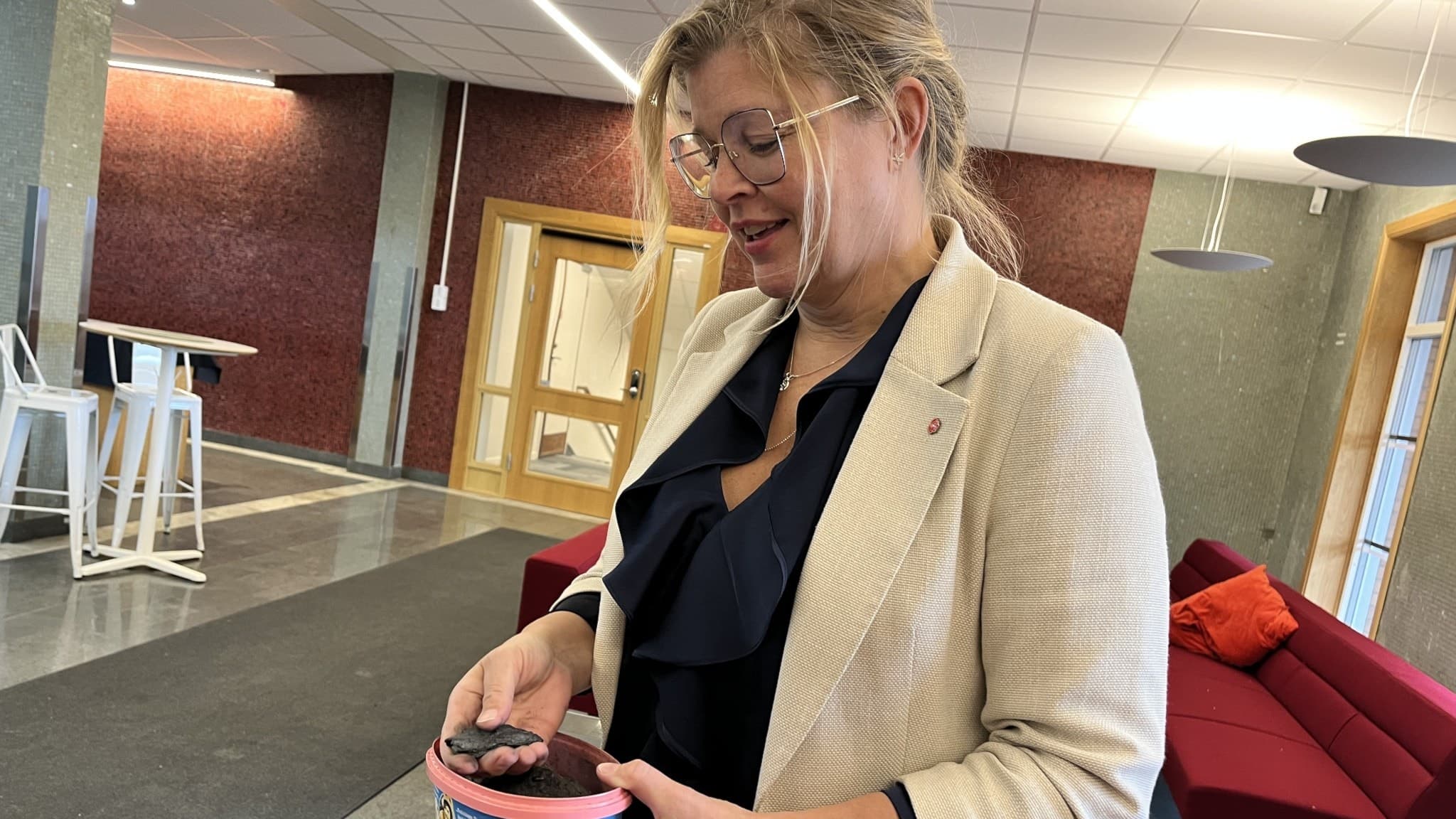 Therese Kärngard (S), kommunstyrelsens ordförande i Bergs kommun, står inomhus i en modern lokal med röda soffor och gråa väggar, iklädd ljus kavaj och mörk blus.