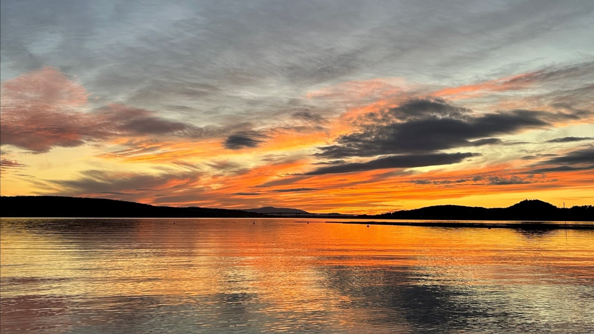 En färgsprakande solnedgång över Minnesgärde i Östersund, med himlen i orange och rosa nyanser som speglas i det stilla vattnet. En nyhetshöjdpunkt från P4 Jämtland.