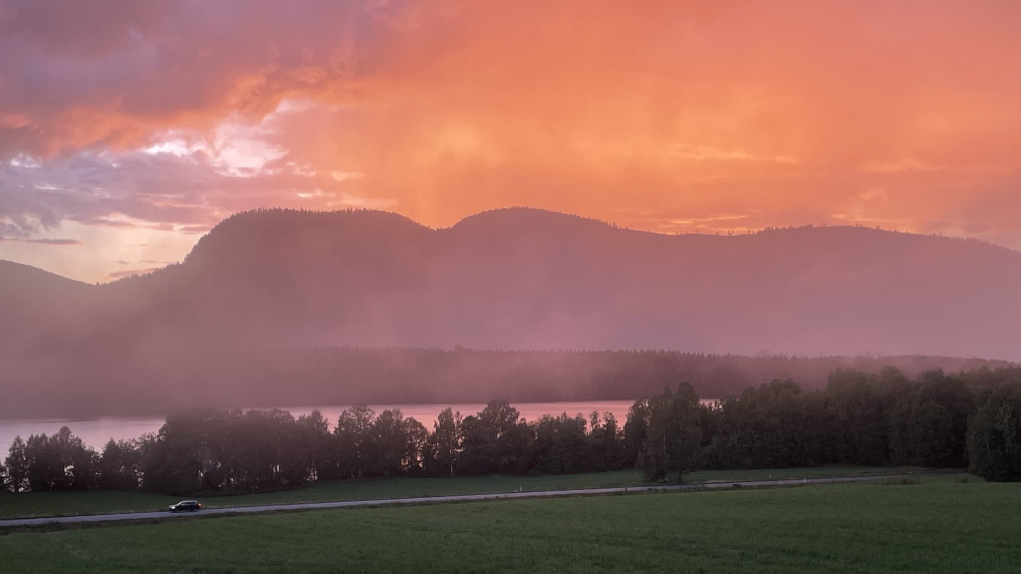 Vättaberget avbildat i ett dramatiskt skymningsljus med rosa och orangea nyanser på himlen, dimma som sveper över landskapet och en skogsklädd siluett i bakgrunden.