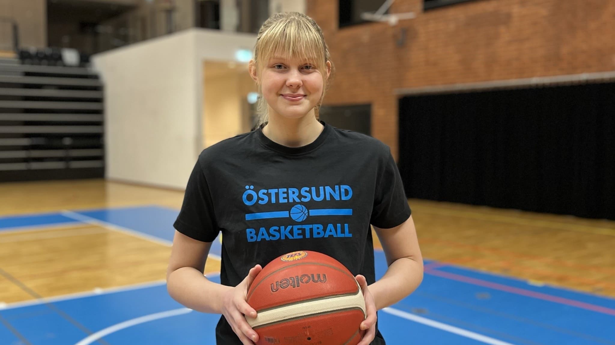 En kvinnlig basketspelare från Östersund Basket står i en sporthall i Östersund och håller i en basketboll. 