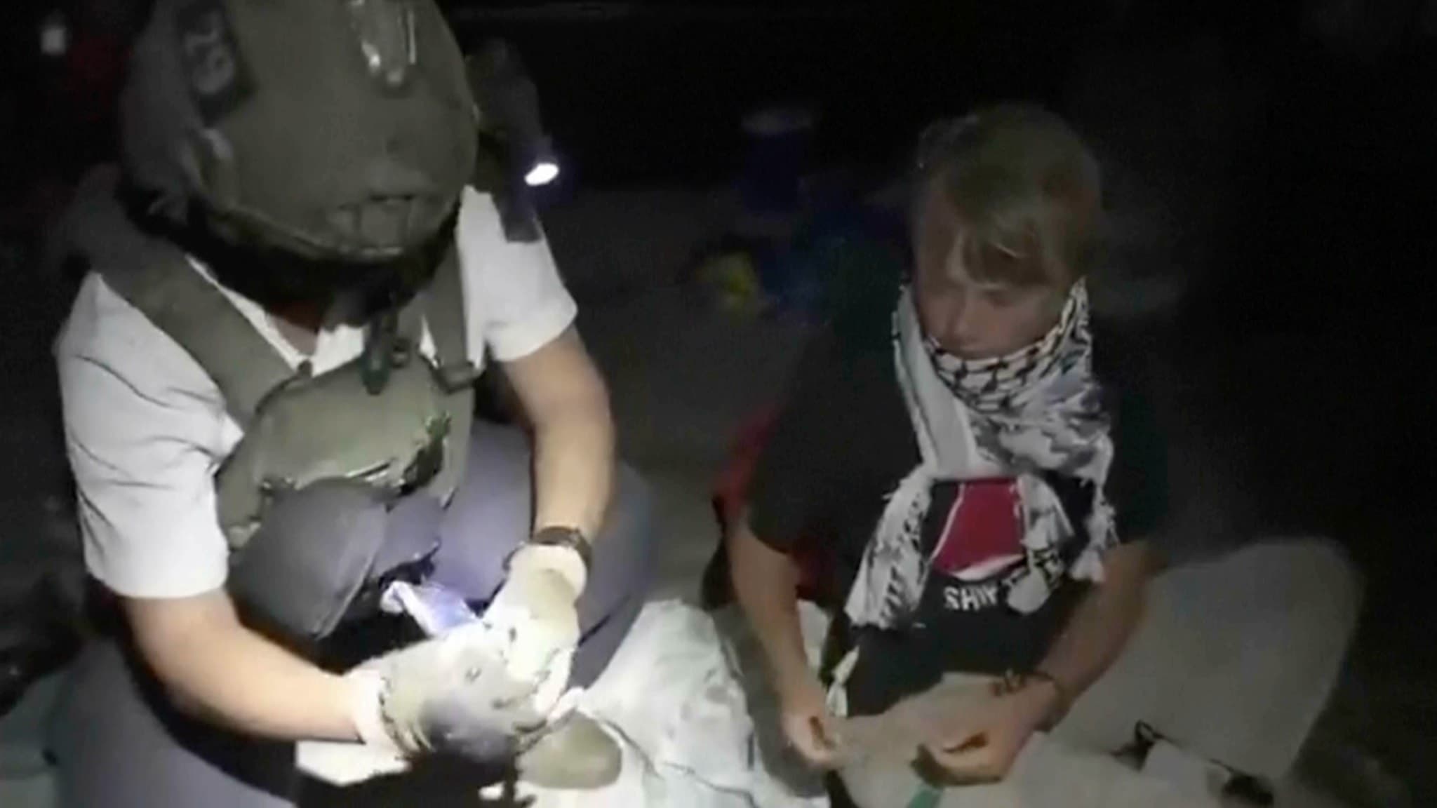 Greta Thunberg ses sittande på marken iklädd en palestinsk halsduk, bredvid en israelisk soldat i uniform med hjälm, efter att ha tagits om hand av israelisk militär på ett fartyg nära Gaza.