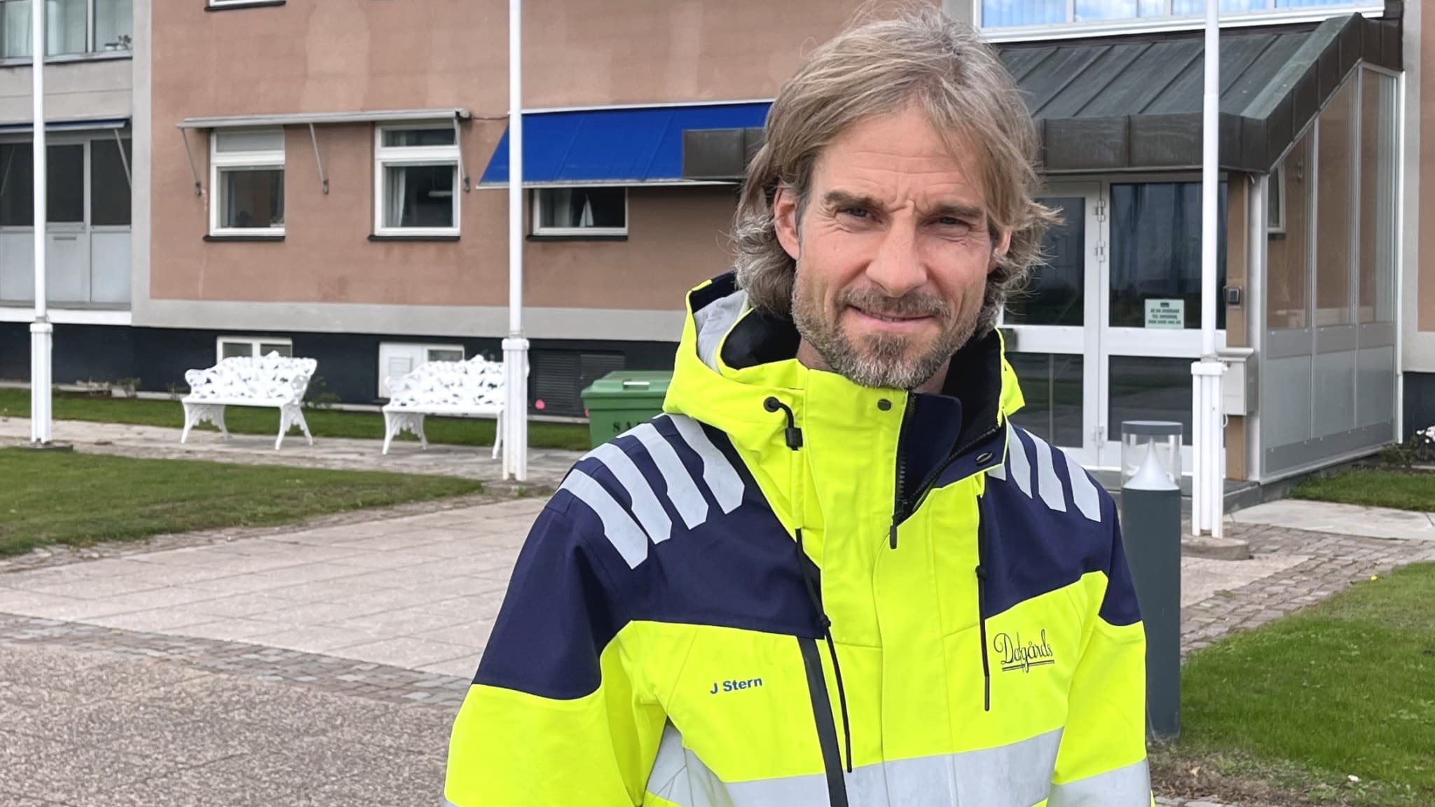 Johan Stern, kvalitet- och hållbarhetsdirektör på Dafgårds, står utomhus klädd i en gul och blå varseljacka framför en byggnad med stora fönster och en grön gräsmatta.