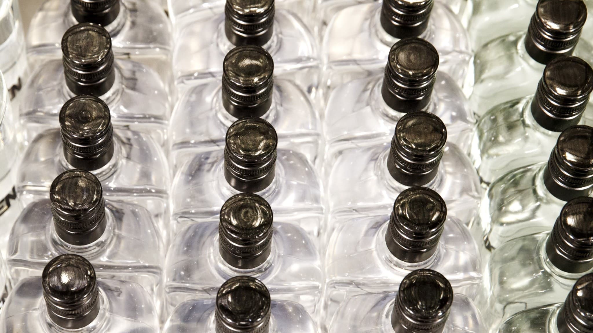 En rad med små flaskor med sprit, tätt packade och staplade. Flaskorna har svarta korkar och genomskinligt glas. Bilden kan illustrera ämnen som alkoholförsäljning eller fulsprit.