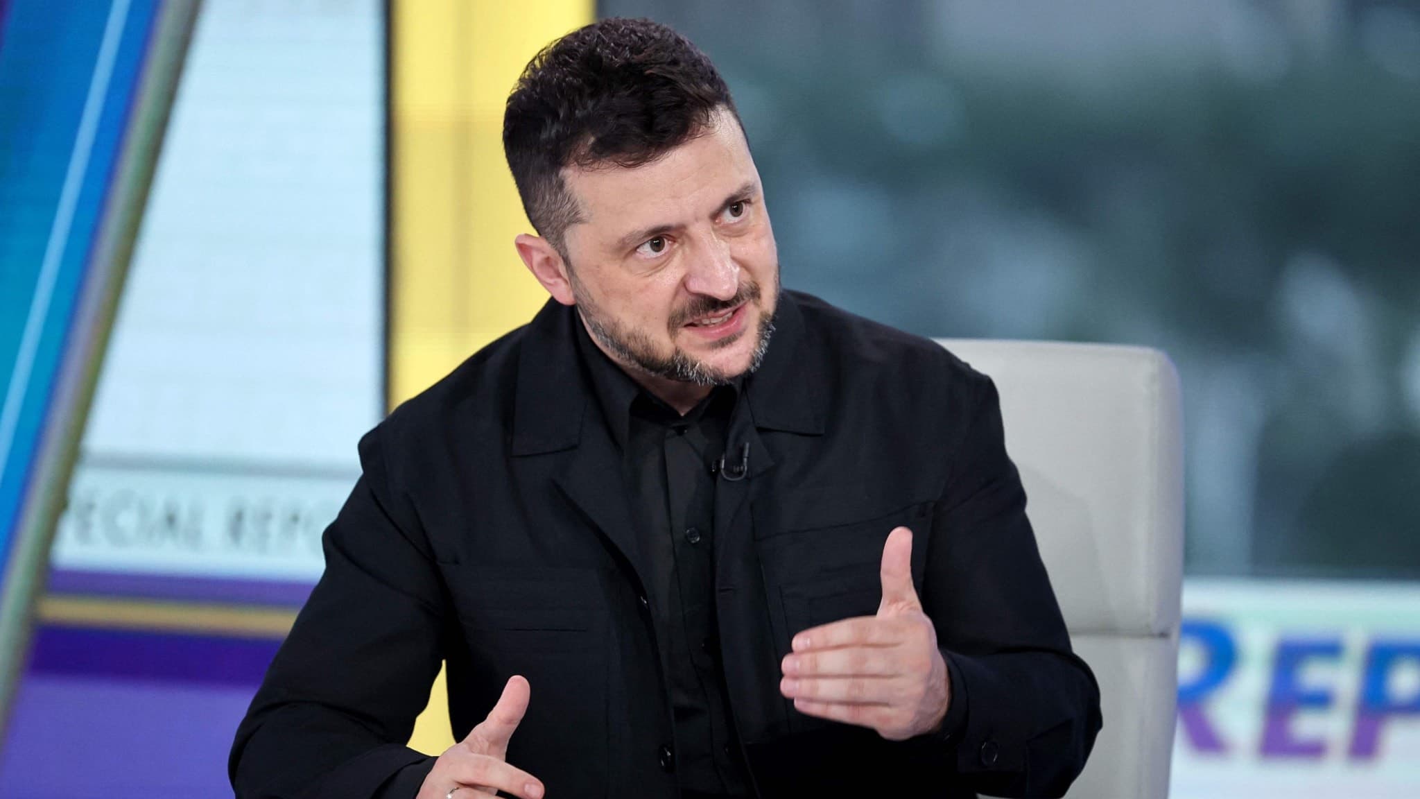 Ukrainas president Volodymyr Zelenskyj sitter vid ett bord i en tv-studio och gestikulerar med ena handen under en intervju.
