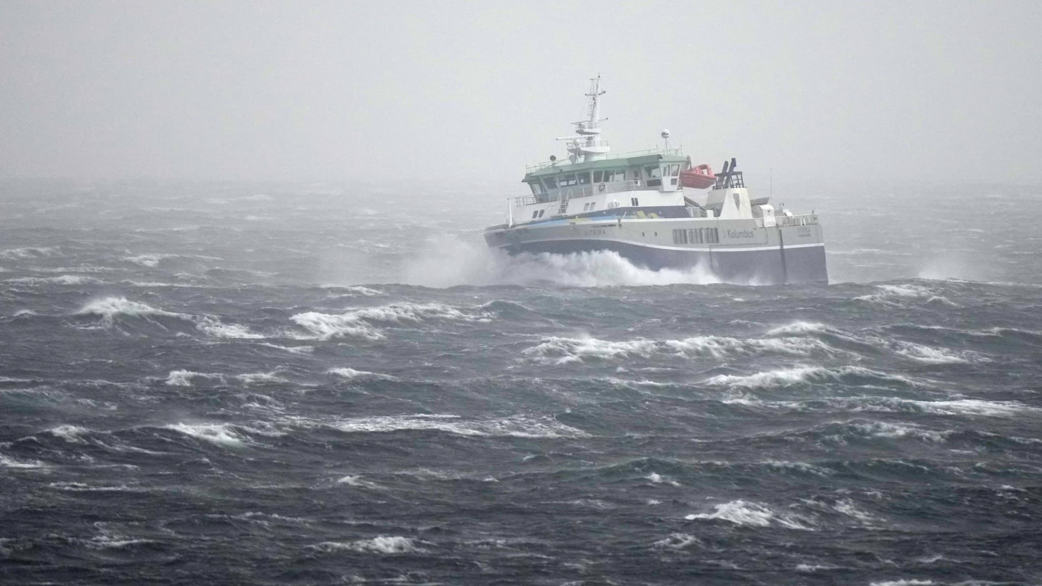 Färjan M/S Utsira navigerar genom kraftigt oväder med höga vågor nära Utsira under ekstremværet Amy. Himlen är grå och havet stormigt, vilket visar vädrets intensitet.