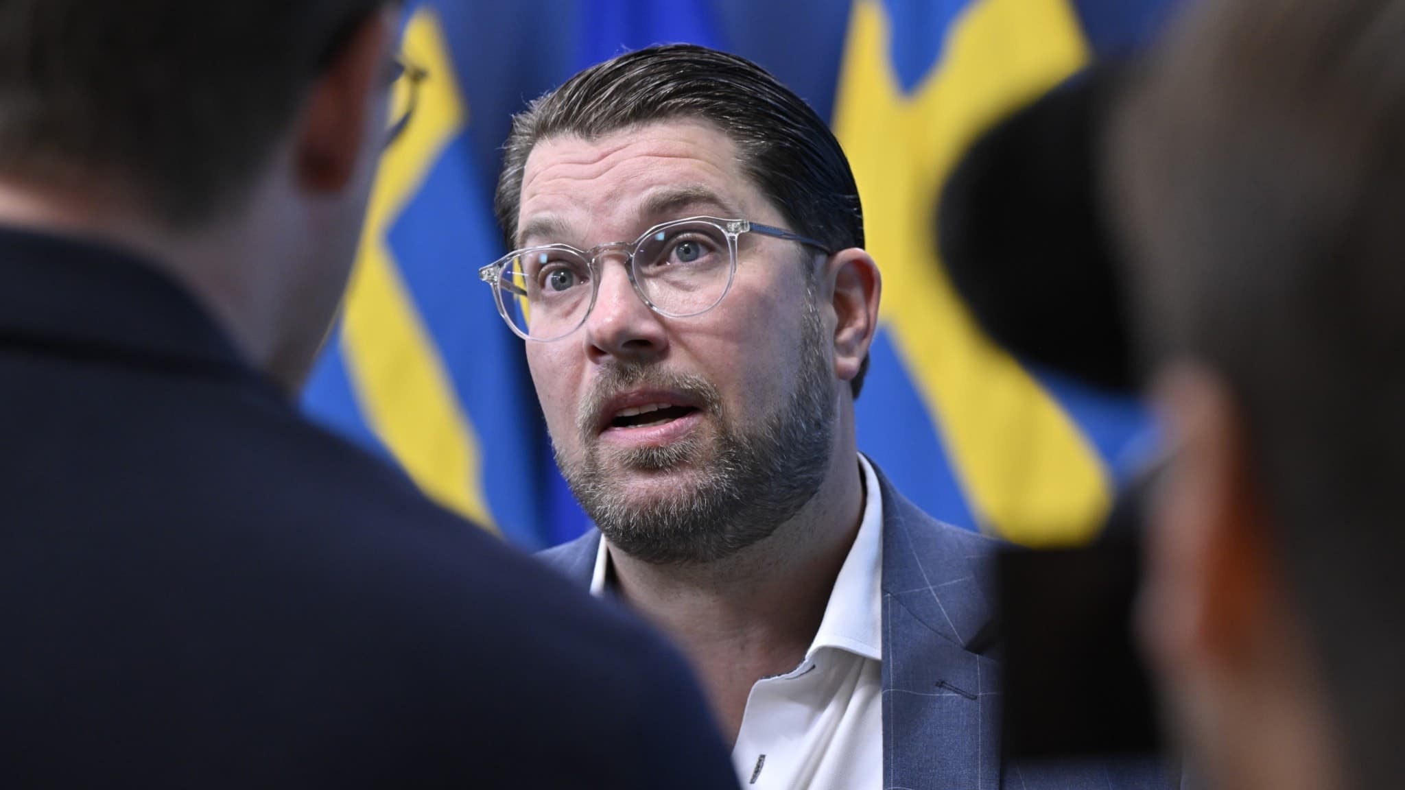 Sverigedemokraternas partiledare Jimmie Åkesson talar under en pressträff i Stockholm om en nyhet kopplad till den kommande höstbudgeten, med svenska flaggor i bakgrunden.