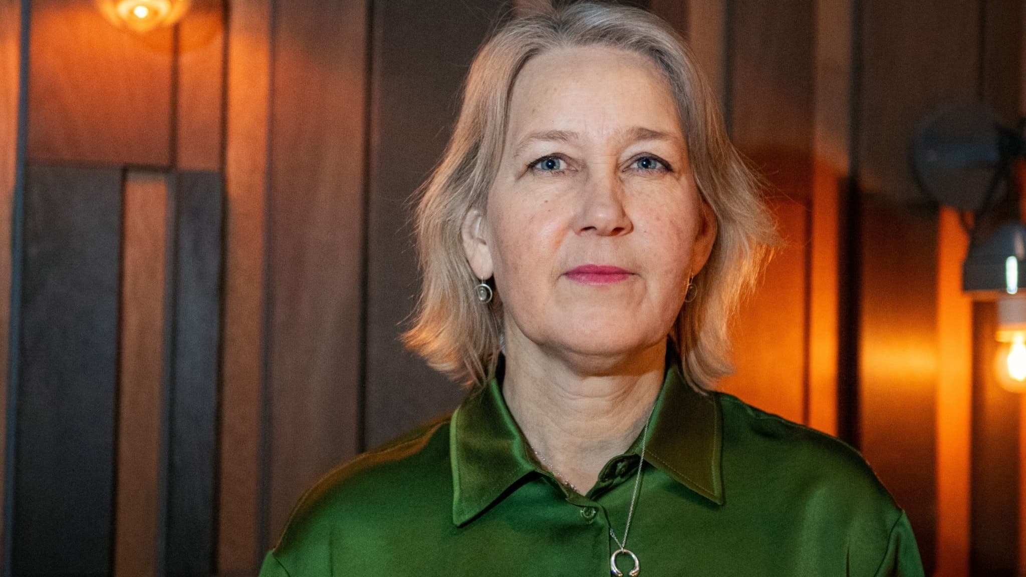 Ulrika Modéer, assisterande generalsekreterare på FN:s utvecklingsprogram, står framför en trävägg med varm belysning. Hon bär en grön skjorta och har kort blont hår.
