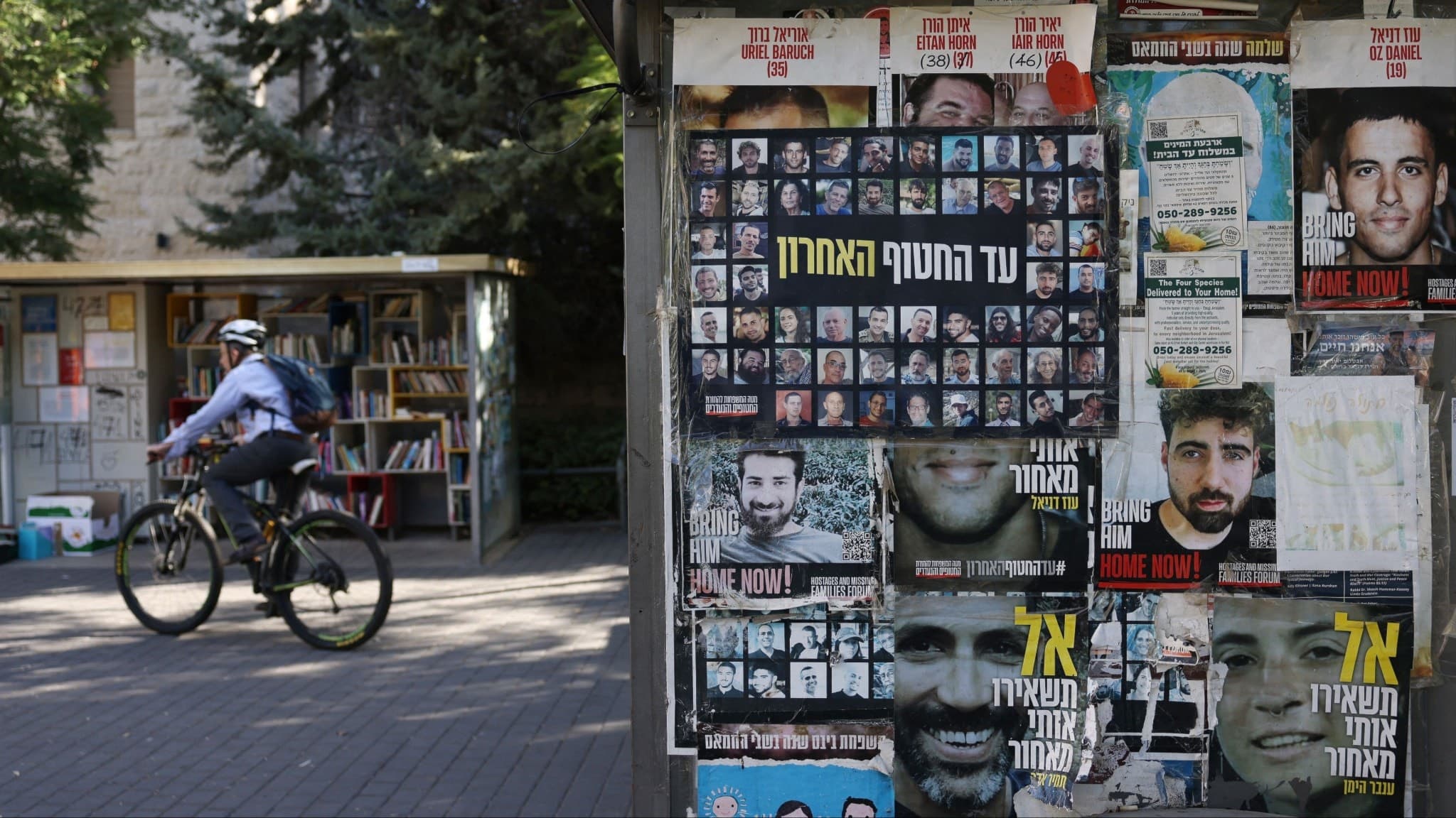 En cyklist bredvid en tidningskiosk i Israel med bilder på gisslan på