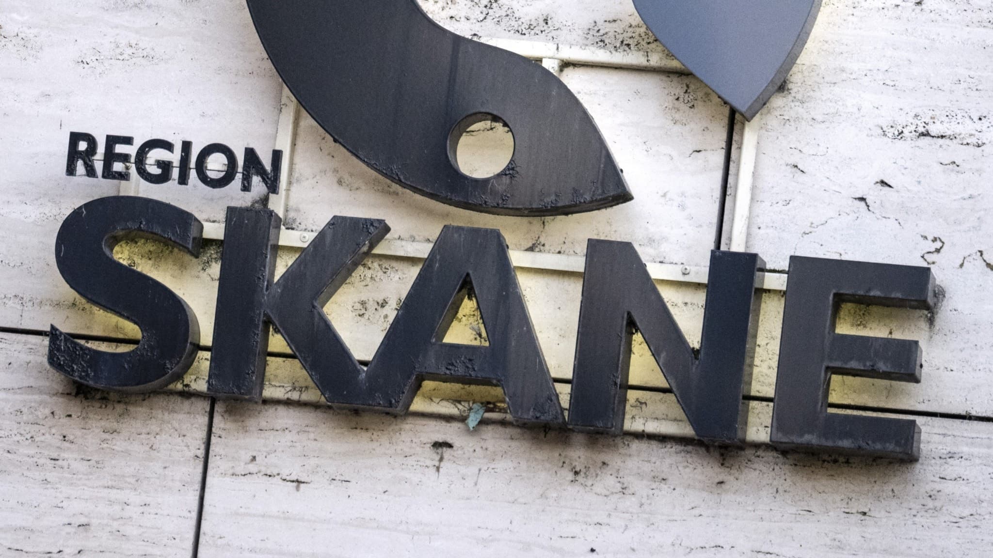 Region Skånes logotyp, med text och en stiliserad symbol, pryder fasaden på Rådhus Skåne vid Stora Torg i Kristianstad. Logotypen är tydligt framträdande mot den ljusa stenfasaden.