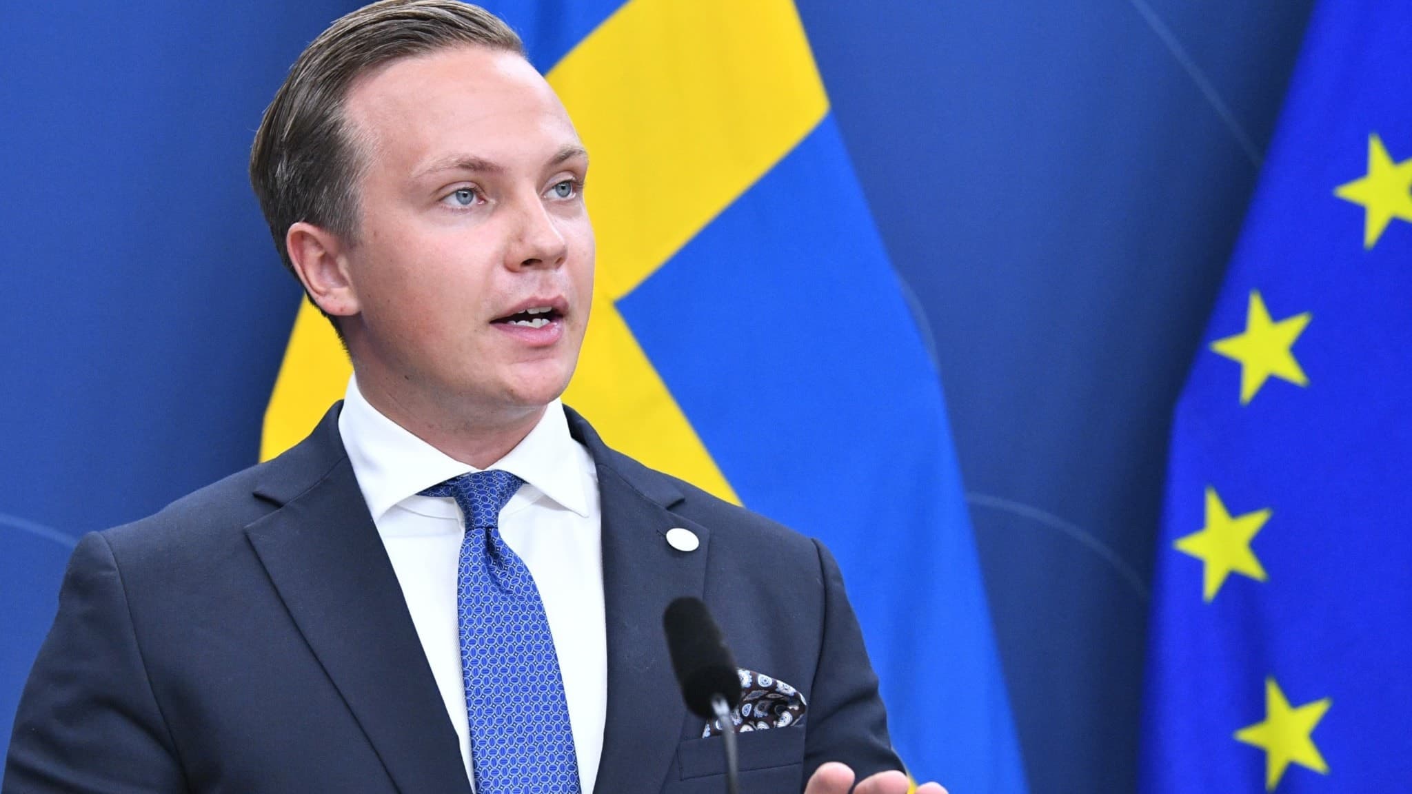 Man med bakåtslickat hår gestikulerar vid en presskonferens. 
